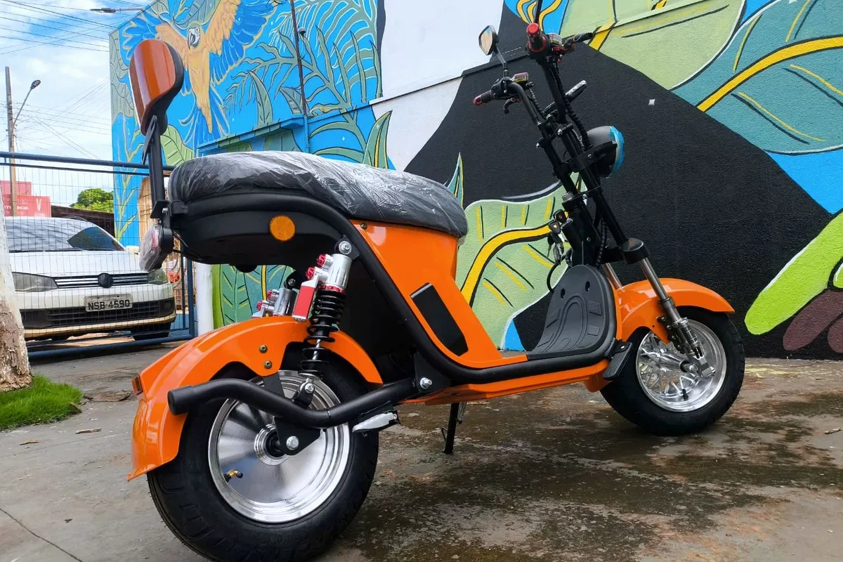 Scooter elétrica laranja em frente a um muro grafitado